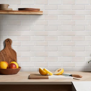 May include: A wall covered in light beige rectangular subway tiles arranged in a brick pattern. A wooden shelf holds a bowl with citrus fruits, while a wooden cutting board on the counter features sliced yellow melon and a metal kitchen knife.