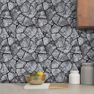 May include: A gray stone wall with irregular shapes and black grout lines. A gold-colored bowl holds a lemon and an avocado. A wooden cutting board and white jar are also visible.