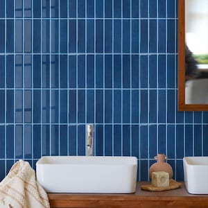 Peut inclure: Une salle de bain moderne avec un mur carrelé bleu, un lavabo rectangulaire blanc et un comptoir en bois. Un robinet chromé est monté sur le lavabo. Un petit vase, un savon et un gant de toilette sont sur le comptoir. Un miroir encadré de bois est à droite.