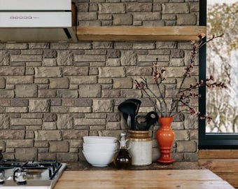 May include: A kitchen countertop with a brown wood surface. A gas stove with a black top and silver trim is on the left side of the counter. Three white bowls are stacked on the right side of the counter. A brown ceramic jar with a lid is next to the bowls. A clear glass bottle with a cork stopper is next to the jar. A red vase with a branch of dried flowers is on the counter. The background is a wall with a brown brick pattern.