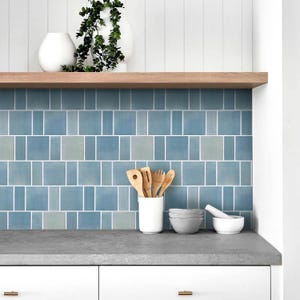 May include: A kitchen backsplash featuring blue and grey ceramic tiles. The tiles are arranged in a staggered pattern. There are wooden utensils in a white ceramic container on the counter.