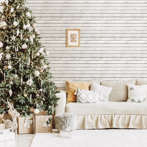 Può includere: Un divano bianco con una gonna a balze bianca si trova di fronte a un muro di legno sbiancato. Il divano è decorato con cuscini in beige, marrone e bianco. Un albero di Natale decorato con ornamenti bianchi e dorati si trova a sinistra del divano.