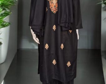 May include: Black embroidered salwar kameez ensemble. The outfit includes a long-sleeved tunic with floral embroidery, matching pants, and a scarf. The embroidery features gold, red, and orange accents. The outfit is displayed on a mannequin.