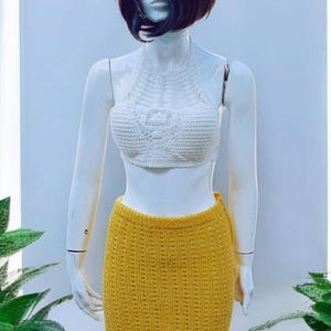 May include: A white crochet halter top and a yellow crochet mini skirt are displayed on a mannequin. The skirt has a ruffled hem. The outfit is handmade and suitable for summer wear.