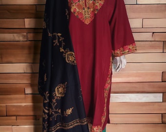 May include: A burgundy embroidered tunic and black shawl displayed on a mannequin. The tunic has detailed floral embroidery in gold, red, and green around the neckline and sleeves. The outfit is completed with green trousers, creating a traditional appearance.