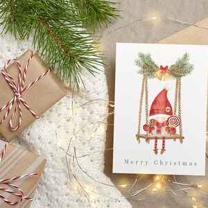 A cute Christmas card featuring a watercolor illustration of gnome, surrounded by festive decorations and winter elements