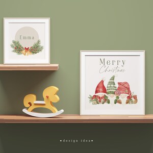 May include: Two framed prints on a wooden shelf. The top print has a green wreath with red berries and gold bells and the text "Emma". The bottom print has the text "Merry Christmas" and a watercolour illustration of three gnomes wearing red and green hats.