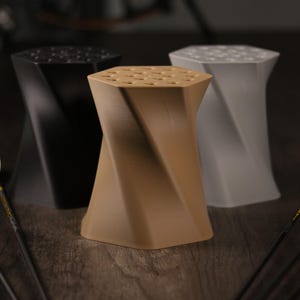 Peut inclure: Trois porte-flèches en plastique imprimé en 3D. Les porte-flèches sont en noir, marron et gris. Les porte-flèches ont la forme d'un sablier tordu. Les porte-flèches sont sur une surface en bois avec des flèches.