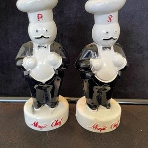 May include: A pair of vintage salt and pepper shakers shaped like chefs. The shakers are white with black accents and have the words "Magic Chef" on the base. The chef on the left has a "P" on his hat and the chef on the right has an "S" on his hat.