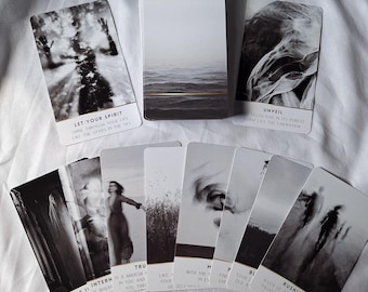 May include: A set of black and white tarot cards with various images and text. The cards are laid out in a fan shape on a white surface. The text on the cards includes "Let Your Spirit Shine Through Your Life Like The Stars In The Sky", "Unveil Truth For In Its Purest Form Lies The Liberation", "Be It Internal", "True", "With The Mirror In Ex", "Find Your Old", "Bl", "Rushing River Of Time Needs To Be Paused To Appreciate The Beauty Of The Journey".