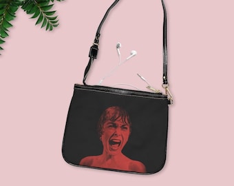 May include: Black crossbody bag with a zip closure. The bag features a red and black image of a woman screaming.