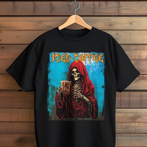 May include: Black t-shirt featuring a graphic of a skeleton in a red hooded robe holding a beverage. The words "Iced Coffee" are printed above the skeleton in a stylized font. The background is blue with a wood-grain texture.