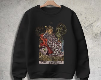 May include: Black sweatshirt with a graphic print of the Empress tarot card. The card features a woman sitting on a throne with a crown on her head. The text "THE EMPRESS." is printed below the image.