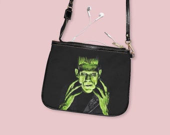 May include: Black crossbody bag with a zip closure and a green and black illustration of Frankenstein's monster on the front.