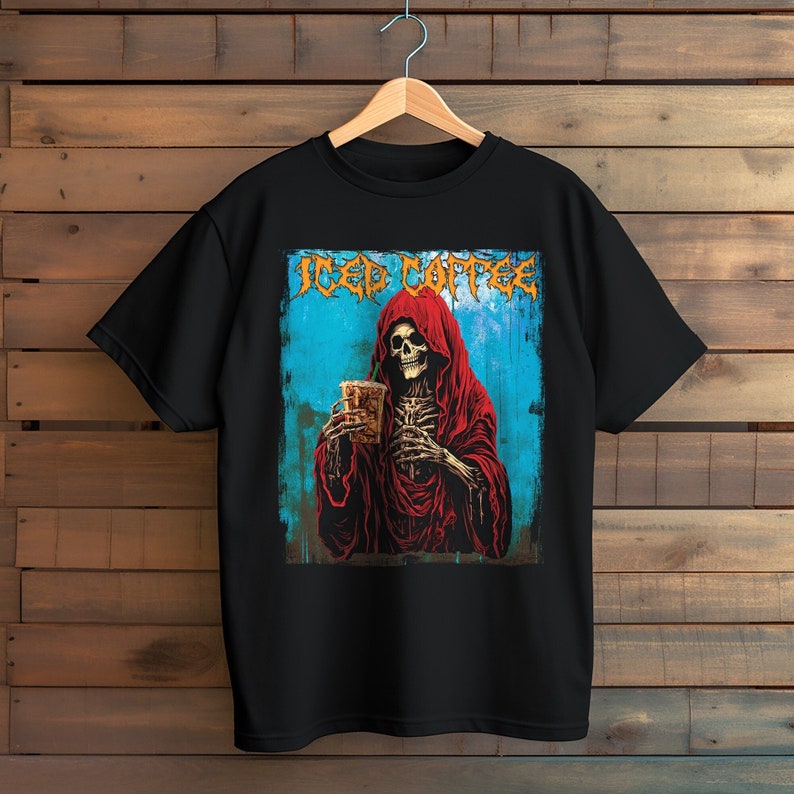 May include: Black t-shirt featuring a graphic of a skeleton in a red hooded robe holding a beverage. The words "Iced Coffee" are printed above the skeleton in a stylized font. The background is blue with a wood-grain texture.