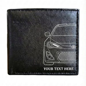 May include: Black leather wallet with a white line drawing of a car's front end. The text "YOUR TEXT HERE" is printed in white at the bottom. The wallet is rectangular and appears to be folded.