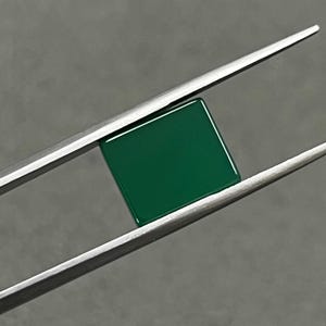 May include: A square, dark green gemstone held by tweezers.