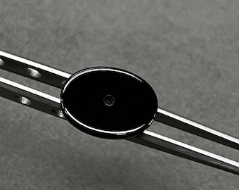 May include: A black oval-shaped button with a small hole in the center. The button is being held by a pair of silver tweezers.