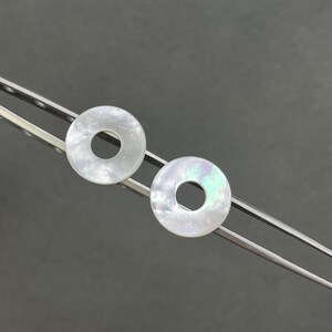May include: Two white iridescent round shell earrings with a hole in the center.