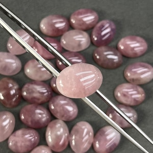 Könnte beinhalten: Eine Sammlung ovaler, rosafarbener Rosenquarz-Cabochons. Die Steine sind glatt und poliert und haben eine durchscheinende Optik.