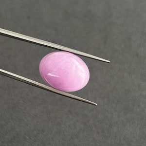 May include: A light pink oval cabochon gemstone held by tweezers.