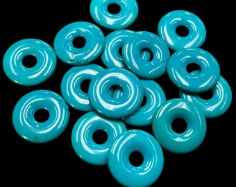 Könnte beinhalten: Eine Gruppe von türkisfarbenen Donut-förmigen Perlen mit einem Loch in der Mitte. Die Perlen sind glatt und glänzend.