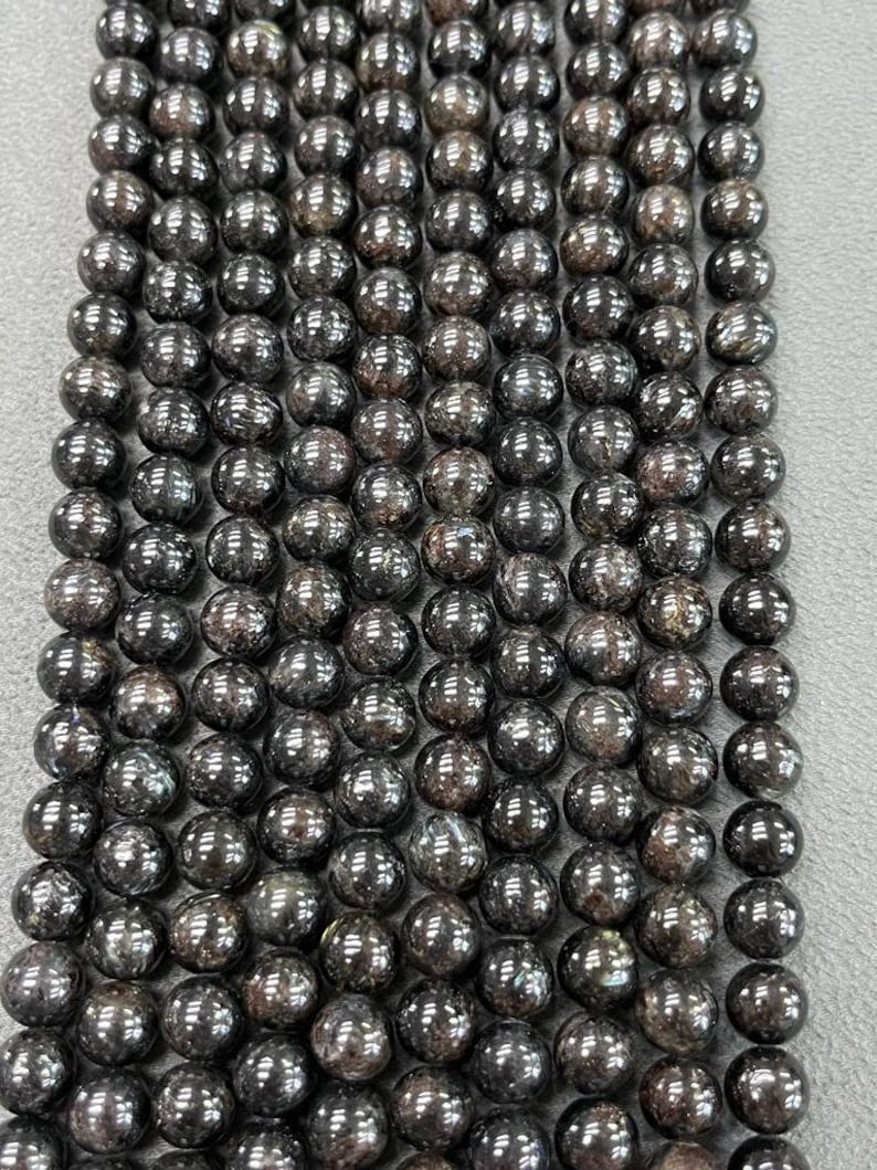May include: A strand of black gemstone beads with a shimmery, iridescent finish. The beads are round and uniform in size, creating a smooth and elegant look.