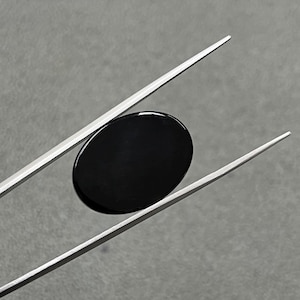 Puede incluir: Una piedra preciosa negra de forma ovalada y cabujón, sostenida por pinzas plateadas.