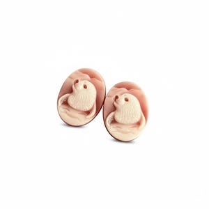 May include: Two oval-shaped cameos featuring a carved cream-colored seal motif set against a soft pink background. Each piece displays a detailed relief of a seal head and flipper, showcasing smooth textures and distinct layered color contrast.