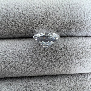 May include: A clear, faceted diamond gemstone on a gray, fuzzy surface.