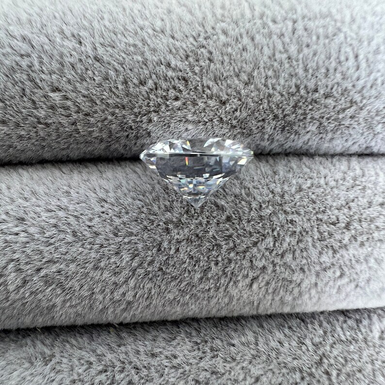 May include: A clear, faceted diamond gemstone on a gray, fuzzy surface.