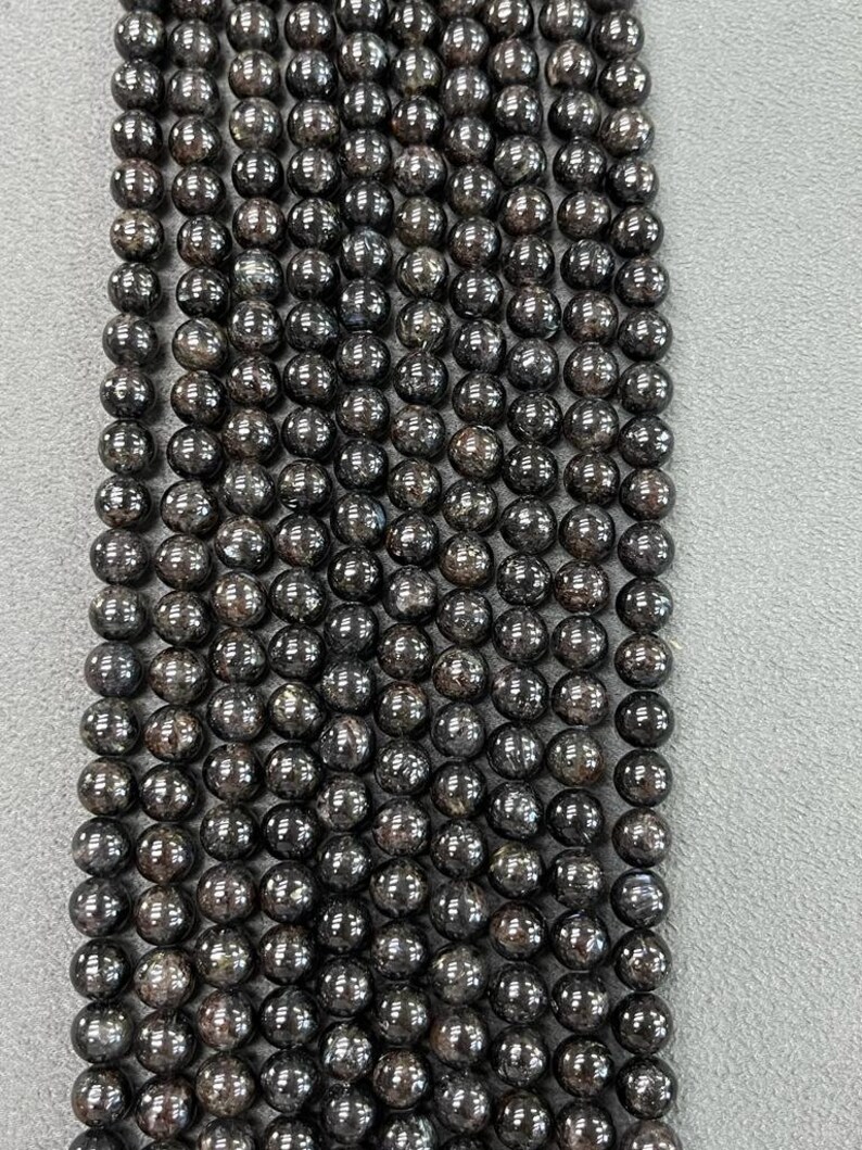 May include: A strand of black round gemstone beads. The beads have a speckled, glittery appearance.