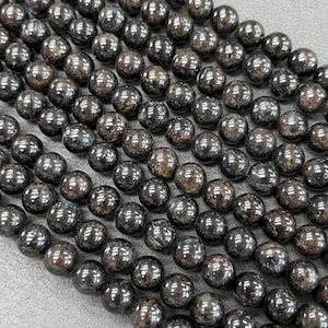 May include: A strand of black gemstone beads with a shimmery, iridescent finish. The beads are round and smooth, and they are strung on a clear thread.