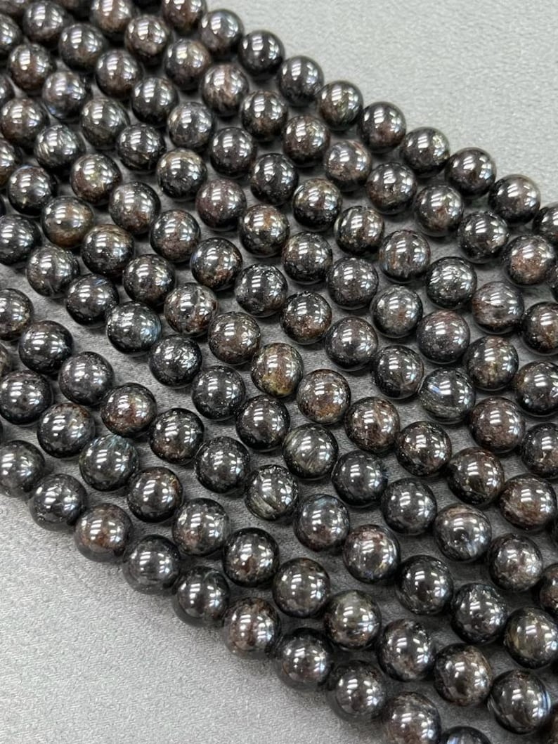 May include: A strand of black gemstone beads with a shimmery, iridescent finish. The beads are round and smooth, and they are strung on a clear thread.
