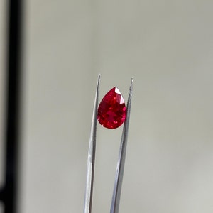 May include: A pear-shaped ruby gemstone held in tweezers. The ruby is a deep red colour and has a high level of brilliance.