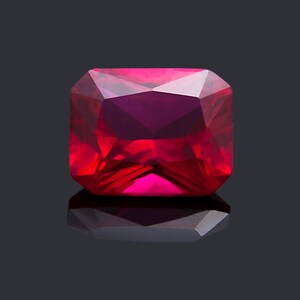 May include: A deep red gemstone with a square cut and a polished finish. The gemstone is reflecting light on a black background.