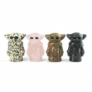May include: Four carved stone figurines of a character with large ears and eyes, in various colors. The figurines include a speckled white and black, a light pink, a green and brown, and a dark gray. The figures are standing upright.