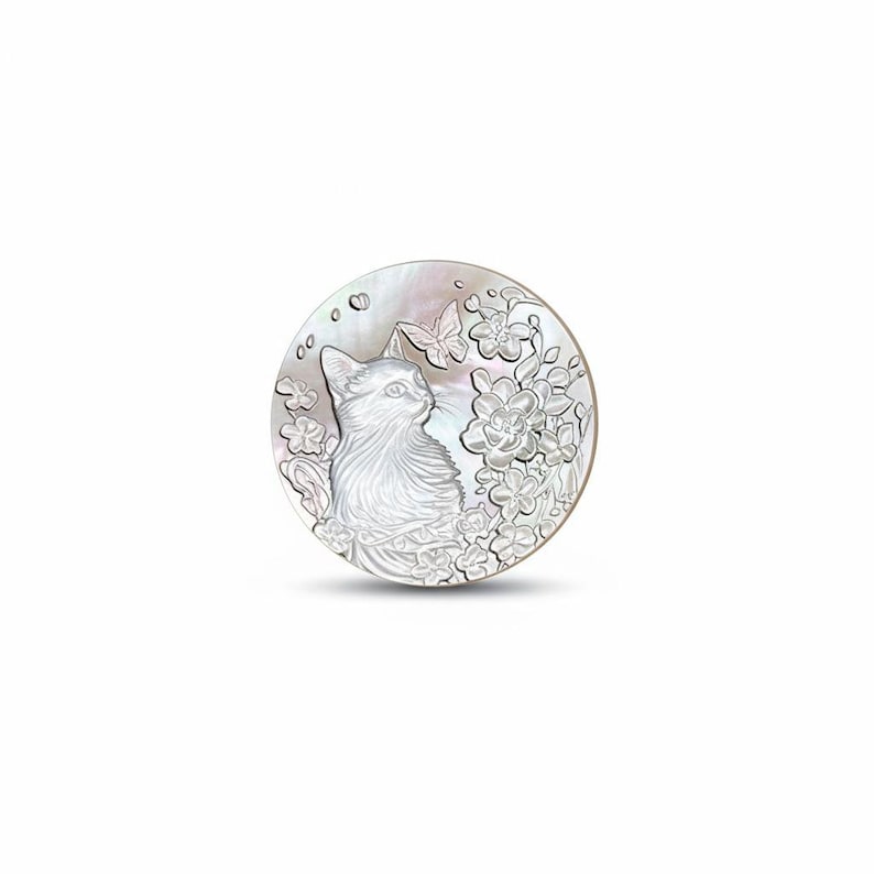 May include: A round, iridescent mother-of-pearl pendant featuring a detailed carving of a cat gazing to the side. The design includes floral elements and butterflies, creating a nature-inspired theme. The pendant has a polished, reflective surface.
