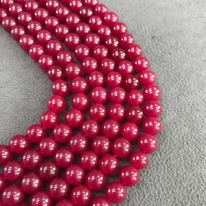 May include: A strand of round, bright pink beads. The beads are smooth and glossy, and they are arranged in a row.