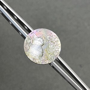 May include: A round, iridescent cat pendant with a floral and butterfly design. The cat is in profile, surrounded by flowers and butterflies. The pendant is set on a silver-colored metal bar.