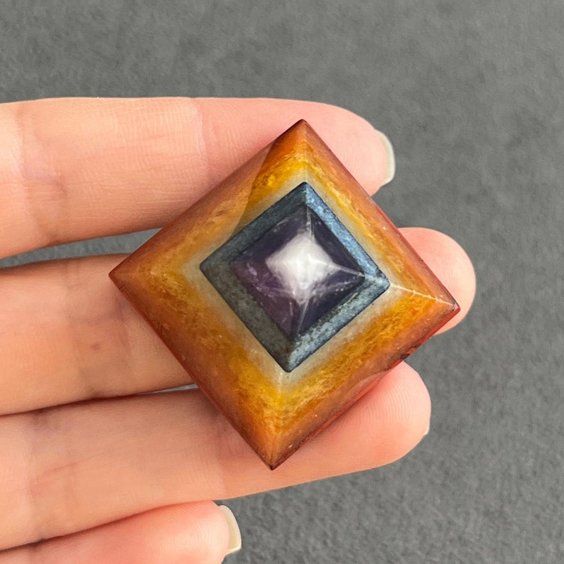 May include: A multi-colored crystal pyramid with a square base. The pyramid is made of layered crystals in shades of orange, yellow, white, purple, and blue. The top of the pyramid is a clear crystal.