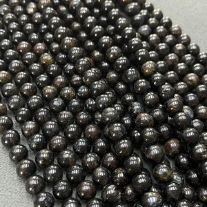 May include: A strand of black gemstone beads with a slight iridescent sheen. The beads are round and smooth, and they are strung on a clear thread.