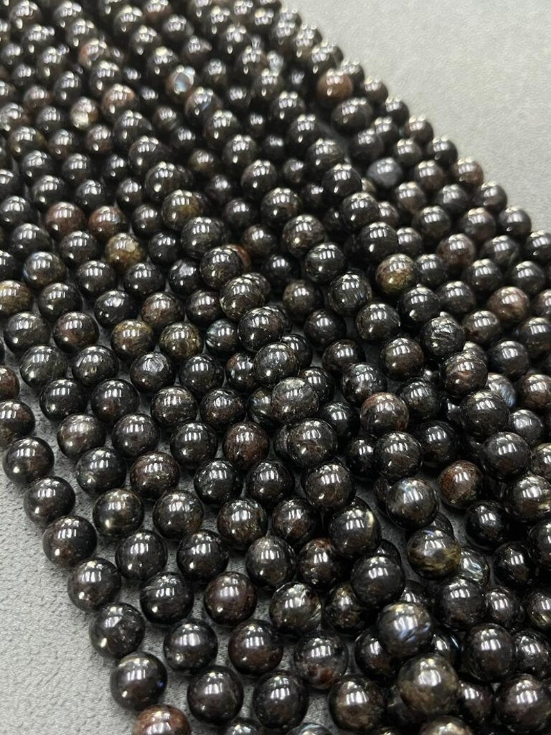 May include: A strand of black gemstone beads with a slight iridescent sheen. The beads are round and smooth, and they are strung on a clear thread.