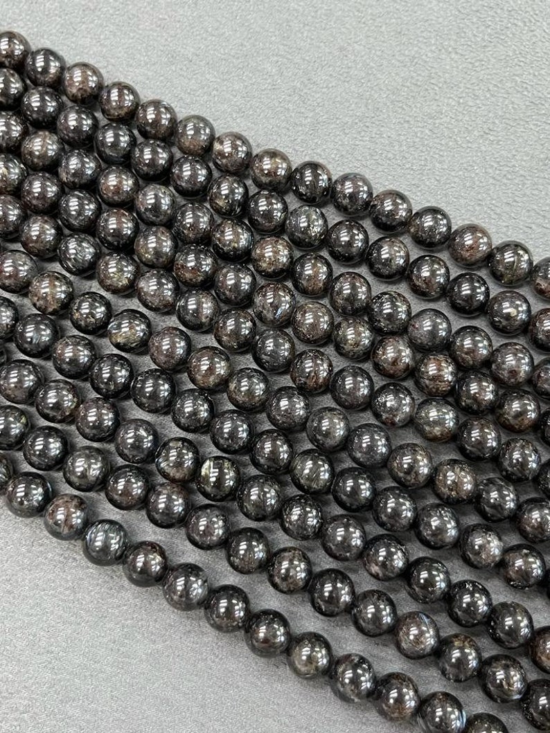 May include: A strand of black gemstone beads with a shimmery, metallic finish. The beads are round and uniform in size, creating a smooth and elegant look.