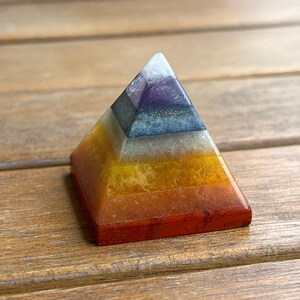 May include: A seven-layered crystal pyramid with a white, purple, blue, gray, yellow, orange, and red base. The pyramid is made of natural stones and is a popular item for meditation and energy healing.