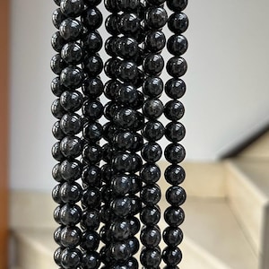 May include: A strand of black gemstone beads, each bead is round and smooth. The beads are strung together on a clear thread.