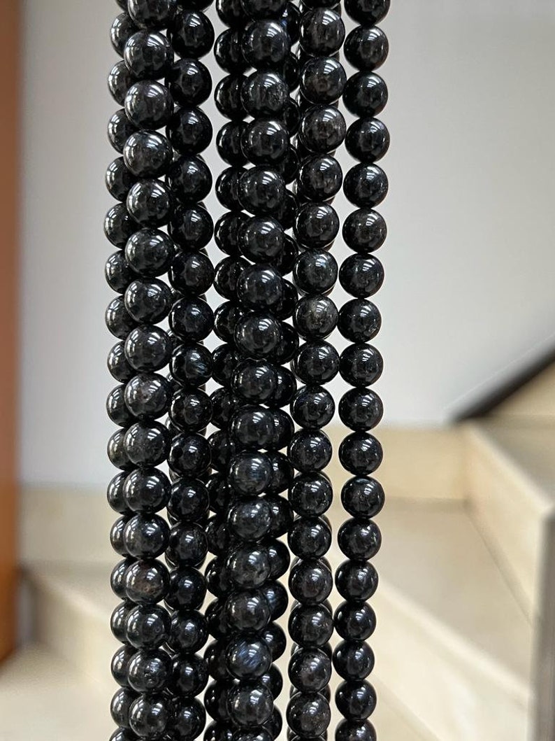 May include: A strand of black gemstone beads, each bead is round and smooth. The beads are strung together on a clear thread.