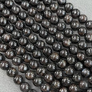May include: A strand of black gemstone beads with a shiny, metallic finish. The beads are round and have a slightly irregular shape.