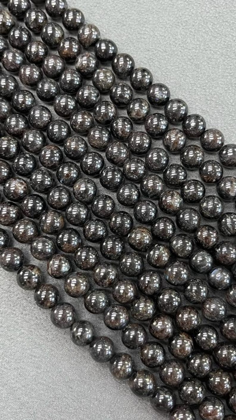 May include: A strand of black gemstone beads with a shiny, metallic finish. The beads are round and have a slightly irregular shape.