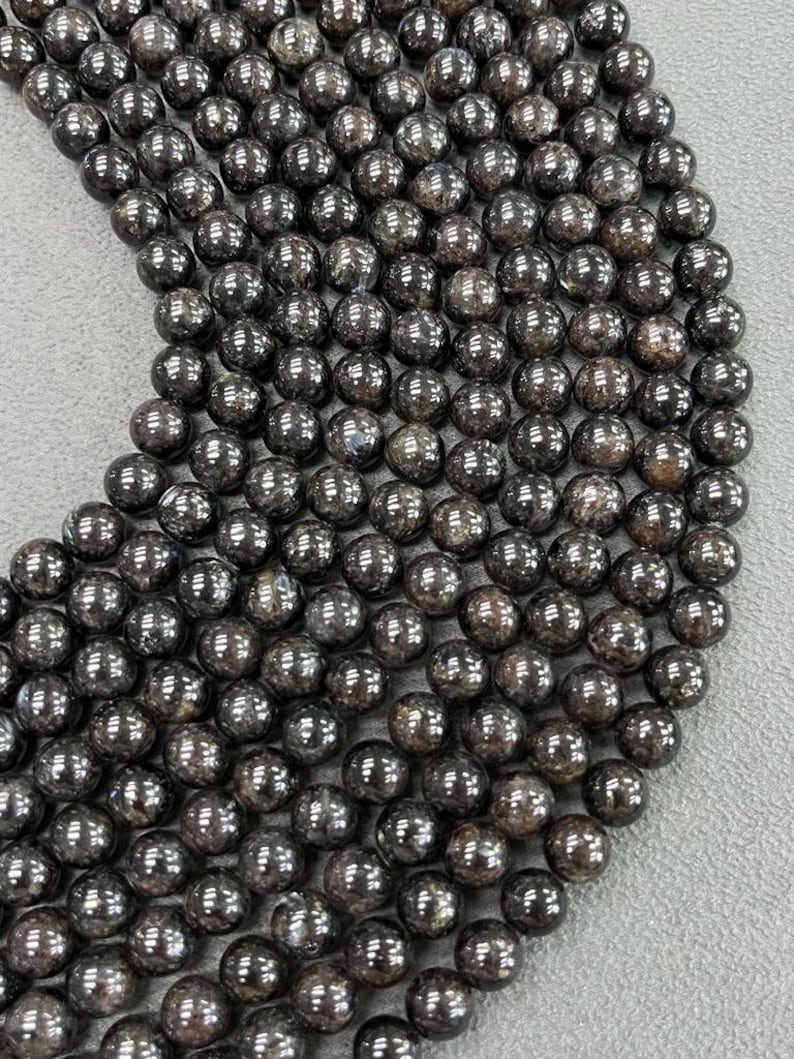May include: A strand of black gemstone beads with a shimmery, iridescent finish. The beads are round and smooth, and they are strung together on a clear thread.